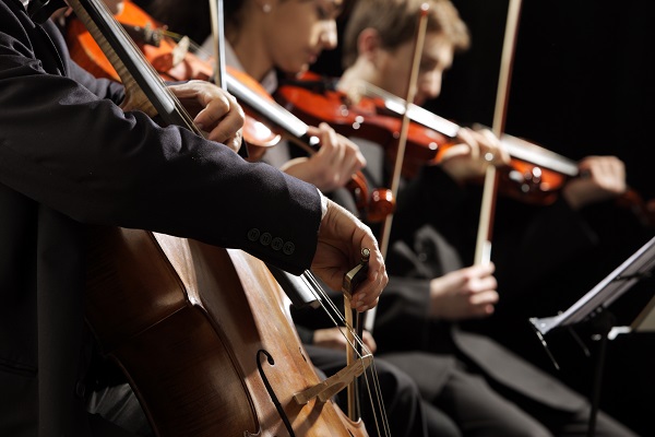 up close of an orchestra strings section: a cellist in the foreground and two violinists in the background