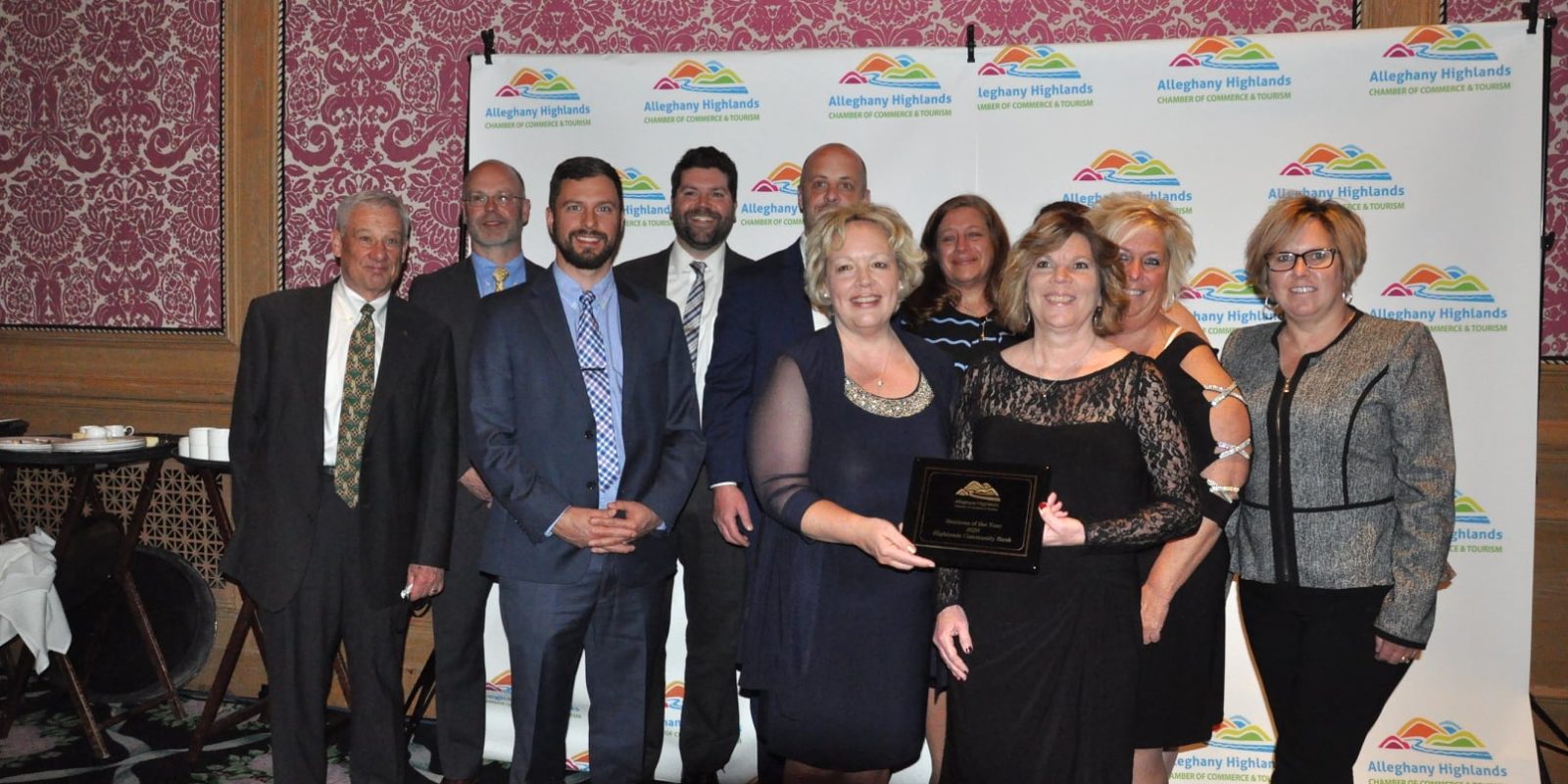 Group of men and women in nice clothes holding a black plaque and standing in front of a white backdrop with the Alleghany Highlands Chamber of Commerce logo