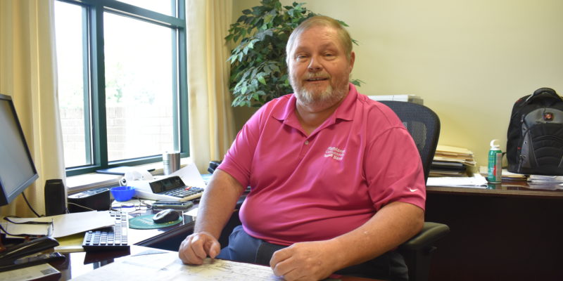 man in pink polo shirt smiling while sitting at desk