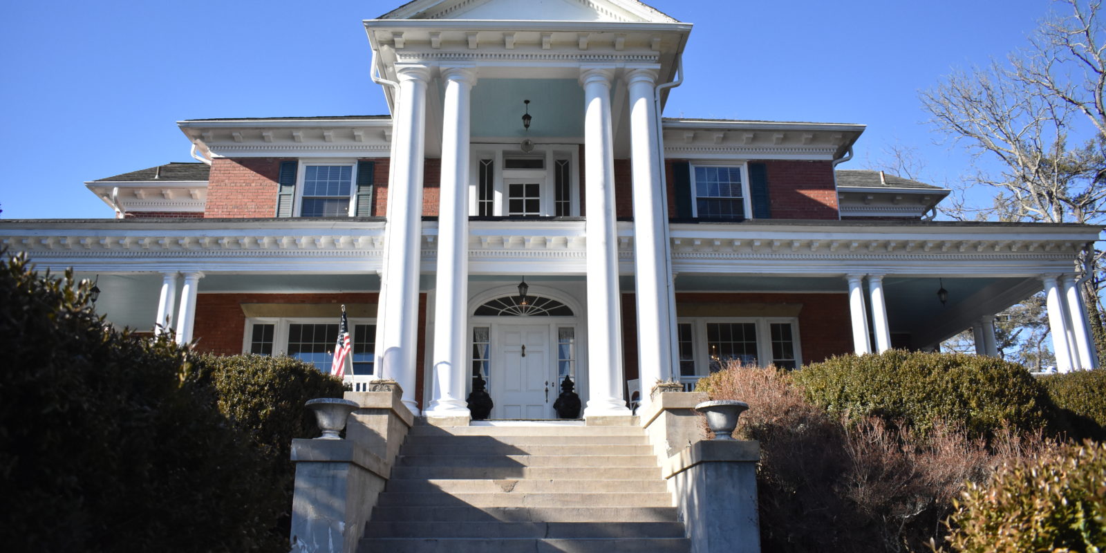 Exterior of front of historic brick building, front stairs lead up to white front door flanked by tall columns