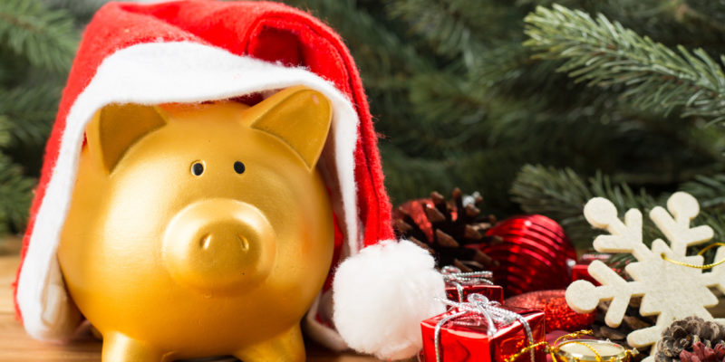 golden piggy banks wearing a santa hat in front of christmas tree branches and ornaments