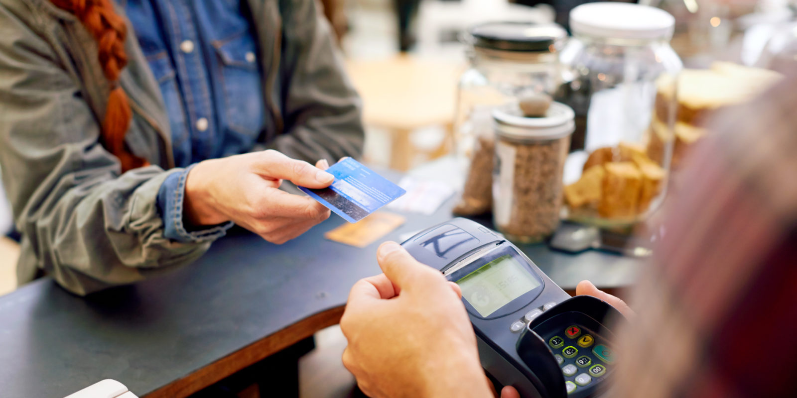 person holds out blue credit card to cashier who is holding a payment terminal