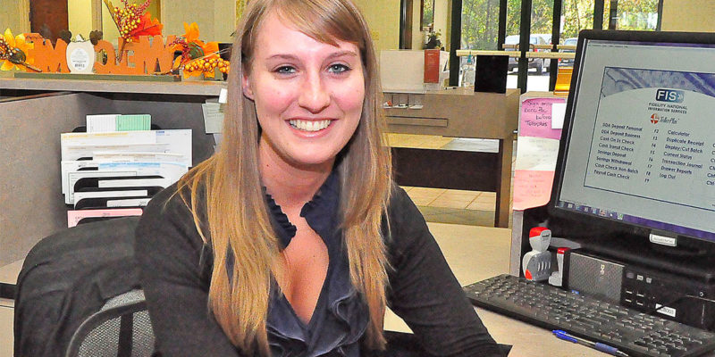 Blonde woman in a black shirt sitting at a computer smiling at the camera