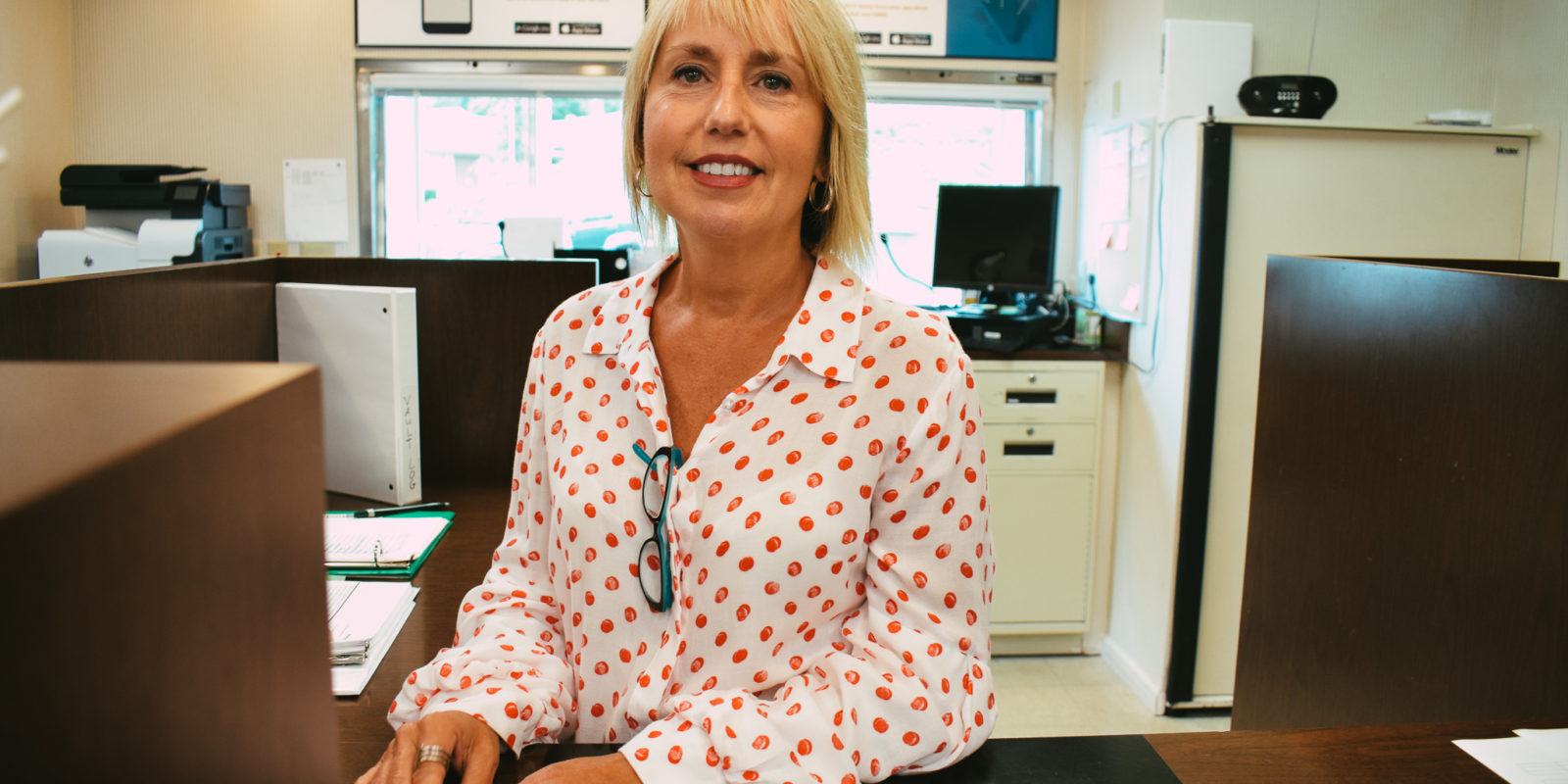 Blonde woman in a white button down shirt with red polka dots smiles at the camera