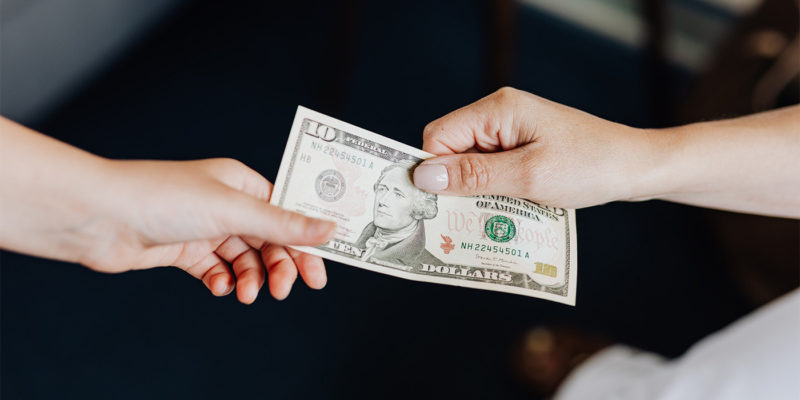 two people's hands holding on to a ten dollar bill