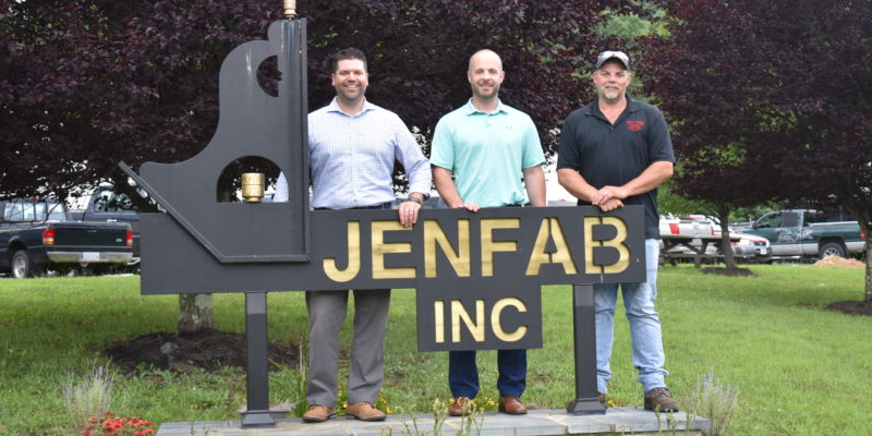Three men stand behind the sign for Jenfab Inc